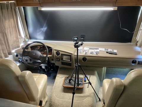 2015 Ford F-550 - The interior of an RV shows the dashboard, steering wheel, and two front seats. A tripod with cameras and various small parts are set up on…