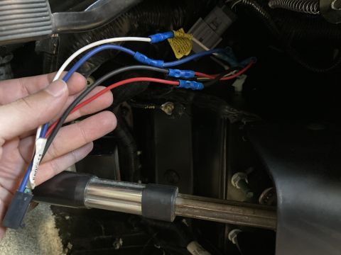 2015 Ford F-550 - A hand holds a bundle of wires with blue, white, black, and red insulation, connected to a black connector. The wires are routed behind a m…