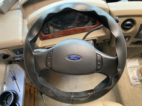 2015 Ford F-550 - Interior view of a Ford steering wheel with a black perforated cover and visible dashboard gauges.