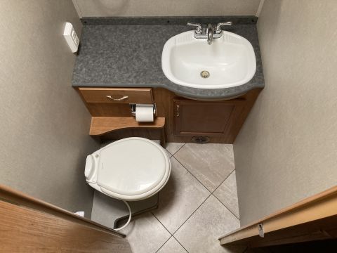 2015 Ford F-550 - Interior view of a compact RV bathroom a toilet, sink, and countertop with a roll of toilet paper dispenser.