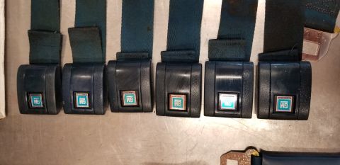1973 Chevrolet Camaro - A collection of six GM seatbelt buckles, each a teal emblem, are laid out on a metallic surface.