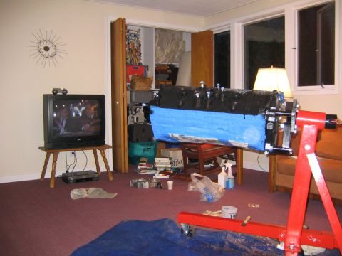 1978 Ford Bronco - An engine block is mounted on a red stand in a room with a television and windows.