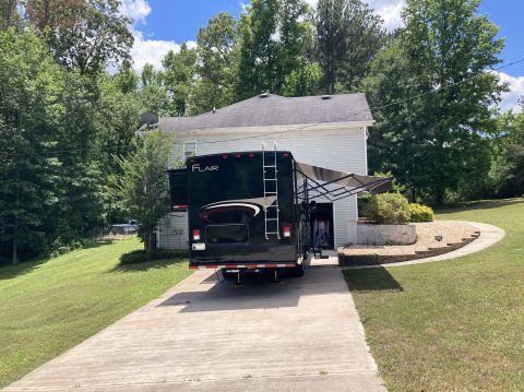 2015 Ford F-550 - The rear of a dark-colored motorhome is visible, parked in a driveway next to a house.