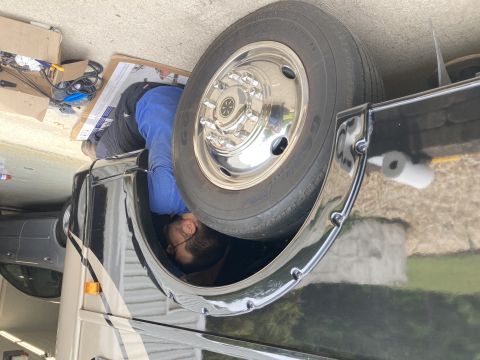 2015 Ford F-550 - A person is working on the wheel well of a large RV, with a spare tire mounted nearby.
