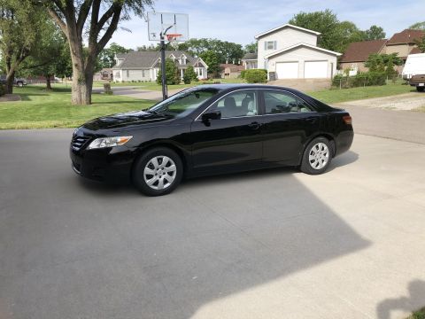 2011 Toyota Camry - A black sedan is parked on a concrete driveway in front of a residential house.