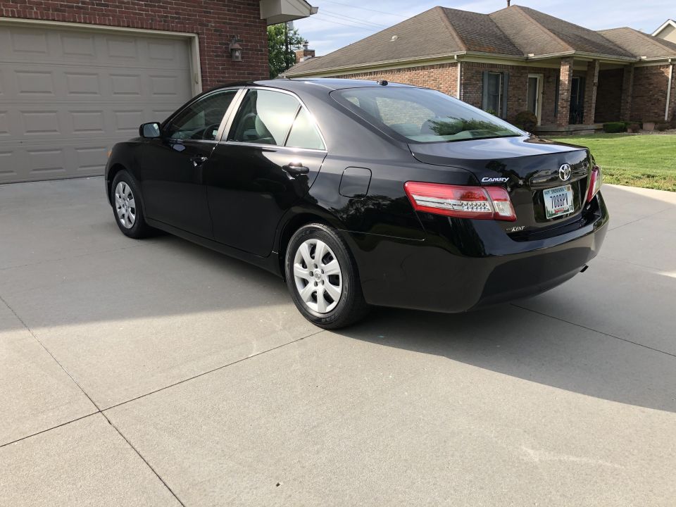 Black Toyota Camry sedan parked on a concrete driveway, rear-left quarter view