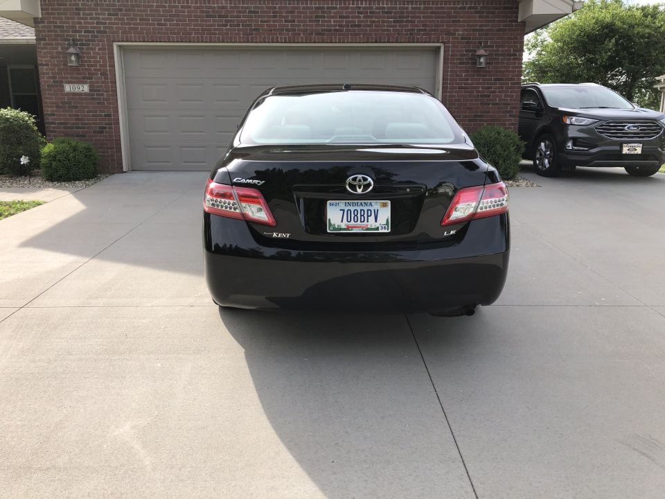 Black 2011 Toyota Camry LE parked in driveway, rear view. Another SUV is parked to the right