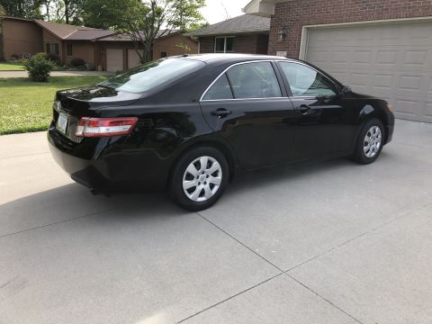 2011 Toyota Camry - A black sedan is parked in a driveway in front of a brick house and garage.