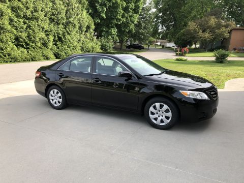 2011 Toyota Camry - A black sedan is parked on a concrete driveway in front of a lawn and trees.