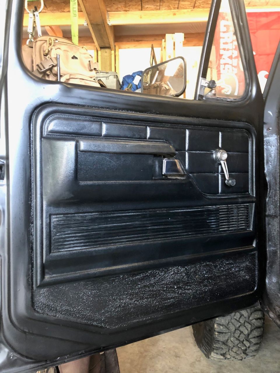 Black interior door panel of a 1978 Ford Bronco with a manual window crank and armrest