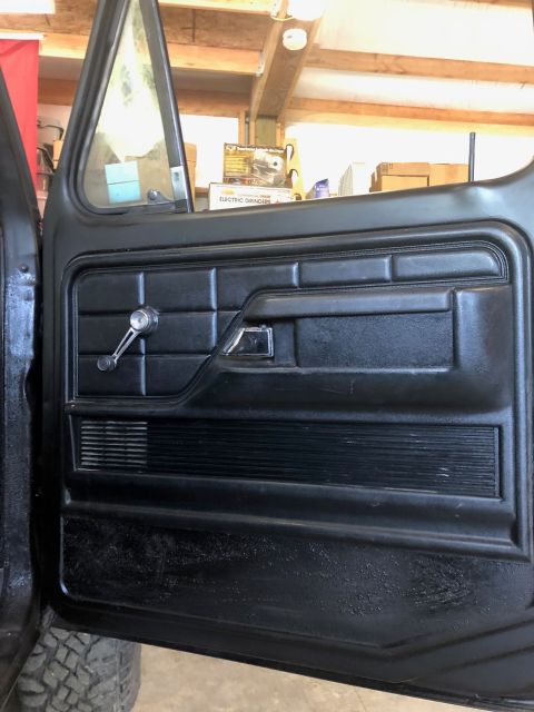 1978 Ford Bronco - Close-up view of a black interior door panel, a chrome window crank and door handle.