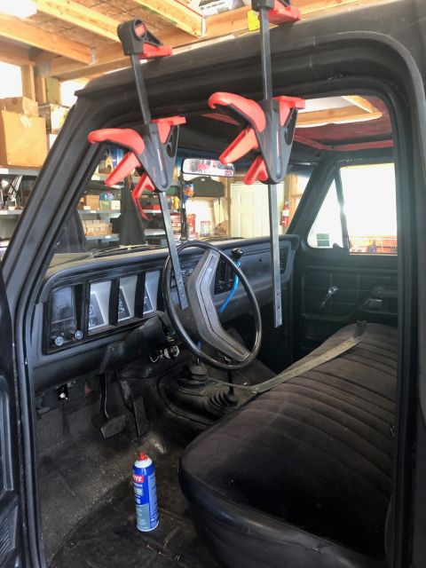 1978 Ford Bronco - The interior of a truck is shown with clamps holding the windshield. A can of lubricant sits on the floor.