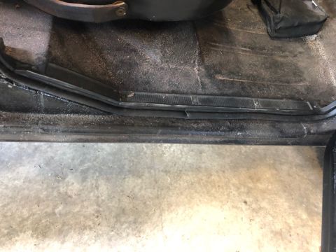 1978 Ford Bronco - The interior door sill and floor of a vehicle appear worn and dirty, with a black bag on the floor.