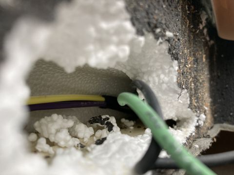 2015 Ford F-550 - Close-up view of wiring bundles passing through a hole in white foam insulation, with a dark textured surface visible to the right.