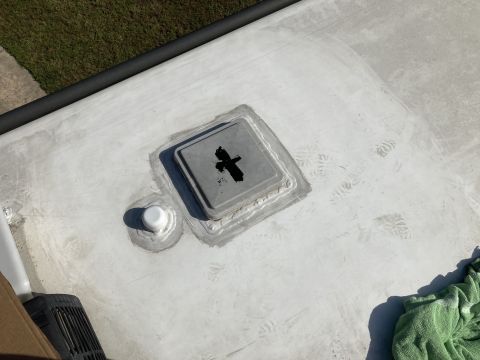2015 Ford F-550 - This is a close-up, high-angle shot of a white RV roof with a gray vent cover and a white pipe fitting, both sealed with sealant. A green t…