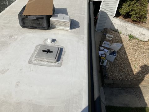 2015 Ford F-550 - A rooftop view of an RV with an air conditioner unit and a vent cover. Various parts and tools are laid out on the ground next to the RV.