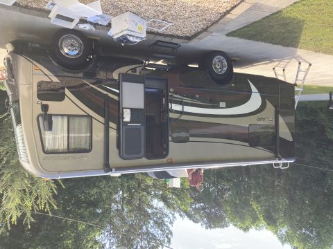 2015 Ford F-550 - A side view of a Fleetwood Flair RV parked on a concrete driveway with a ladder leaning against it. The RV has a tan and dark brown exterio…