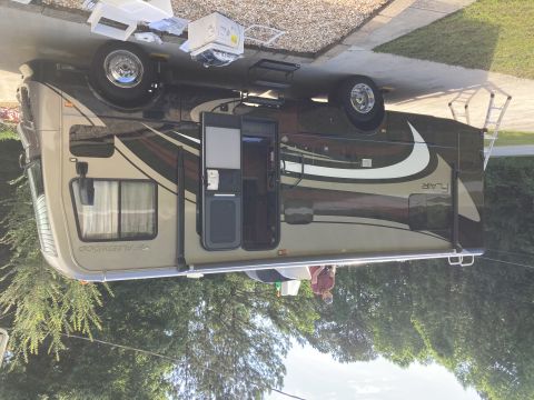 2015 Ford F-550 - A Fleetwood Flair RV is parked on a concrete driveway with a ladder attached to the rear. Several white boxes and parts are on the ground n…