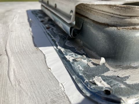 2015 Ford F-550 - Close-up view of a damaged sealant and metal flashing around a roof vent on a white RV roof. The sealant is peeling away, exposing the unde…