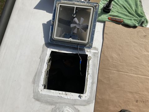 2015 Ford F-550 - A rooftop vent is open and removed from a vehicle, revealing the dark interior opening. The vent assembly, showing a fan, is placed next to…