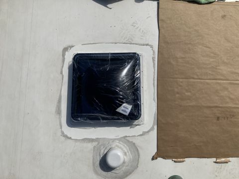 2015 Ford F-550 - A square vent with a plastic film cover is installed on a white roof, surrounded by sealant. A white pipe fitting is also visible below the…