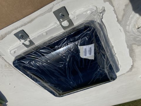 2015 Ford F-550 - A black RV vent cover is installed on a white roof, secured with metal brackets and sealant. The vent cover is still in its protective plas…