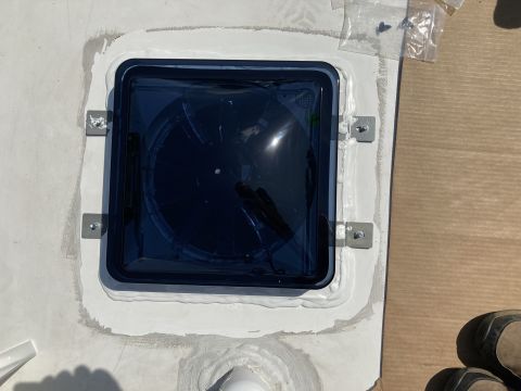 2015 Ford F-550 - A dark tinted RV roof vent is installed on a white roof with sealant around the edges and metal brackets securing it. Several small screws…