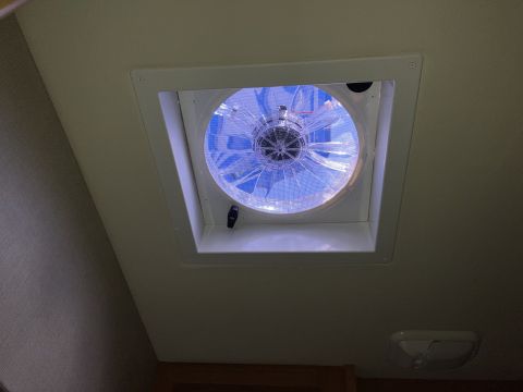 2015 Ford F-550 - A close-up, low-angle view of a white ceiling-mounted RV vent fan with blue LED lights illuminated. A small, white interior light fixture i…