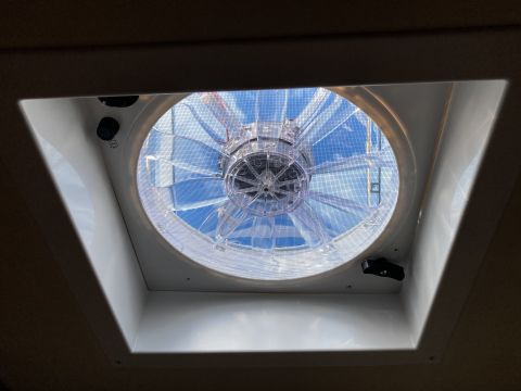 2015 Ford F-550 - A clear plastic fan with a mesh screen is installed in a ceiling vent, looking up towards a blue sky with clouds.
