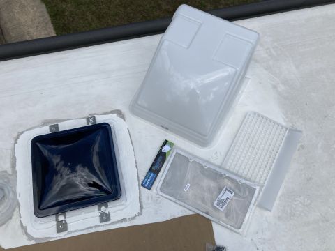 2015 Ford F-550 - A dark blue vent cover is installed on a white RV roof with sealant. Nearby are a white vent cover and several mesh and plastic vent compon…