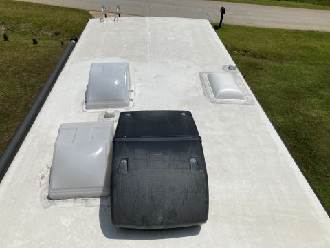 2015 Ford F-550 - The roof of an RV is shown with several fixtures including two white vent covers, a black air conditioner shroud, and a skylight. A dark gr…