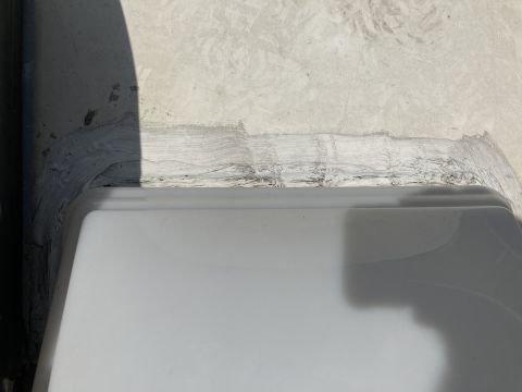 2015 Ford F-550 - A close-up view shows a white RV sink basin with a gray sealant applied around its edge, sealing it to a concrete-like surface. The sealant…