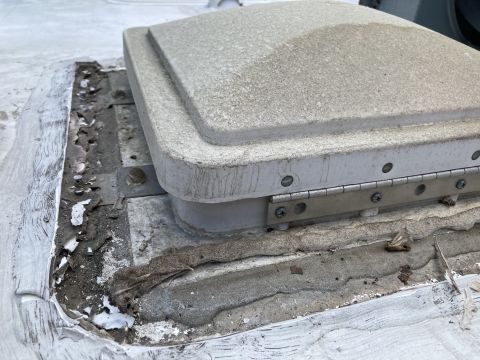 2015 Ford F-550 - A close-up view of a dirty, weathered rooftop vent on a vehicle, showing exposed sealant and a metal hinge.