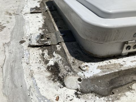 2015 Ford F-550 - Close-up view of a white RV roof vent flange with sealant and metal brackets, showing signs of wear and dirt accumulation.