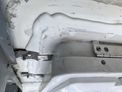 2015 Ford F-550 - A close-up view shows white sealant applied to a seam on a white vehicle, with metal brackets and a hinge visible.