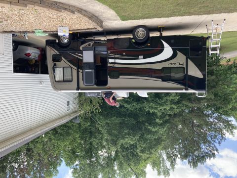 2015 Ford F-550 - A Fleetwood Flair RV is parked in a driveway next to a house. A ladder is propped against the side of the RV.