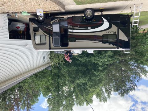 2015 Ford F-550 - A Fleetwood Flair motorhome is parked in a driveway next to a house, with a ladder leaning against the rear. A person is crouching near the…