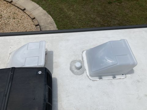 2015 Ford F-550 - Two white vent covers are installed on the white roof of an RV, one partially obscuring a black air conditioning unit. A small white pipe p…
