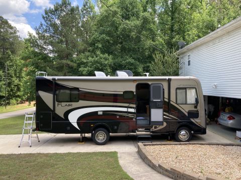 2015 Ford F-550 - A Fleetwood Flair RV is parked on a paved driveway next to a house. The RV has a beige and black exterior with red and white graphics, and…