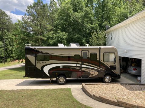 2015 Ford F-550 - A Fleetwood Flair motorhome is parked on a concrete driveway next to a house with an open garage door. The motorhome is tan and dark brown…
