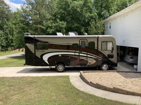 2015 Ford F-550 - A beige and brown Fleetwood Flair motorhome is parked on a concrete driveway next to a house with an open garage. The motorhome is position…
