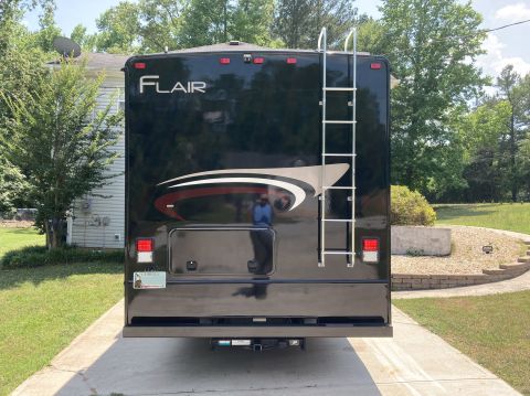 2015 Ford F-550 - The rear of a black Fleetwood Flair motorhome is shown parked on a concrete driveway. A silver ladder is mounted to the rear of the vehicle…