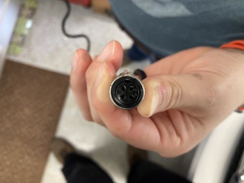 2015 Ford F-550 - A hand holds a circular electrical connector with four pins, suggesting a component rather than a vehicle.