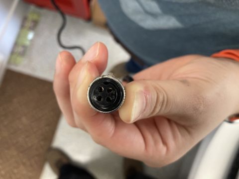 2015 Ford F-550 - A hand holds a circular electrical connector with four pins, likely for a camera or sensor.