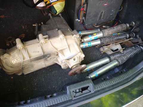1996 Ford Bronco - A transfer case and four Bilstein shock absorbers are laid out in the trunk of a vehicle. A Kicker amplifier is visible in the background.