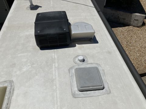 2015 Ford F-550 - The roof of an RV is shown with a black air conditioning unit and a white vent. A gray access panel with a white cap is sealed to the roof.