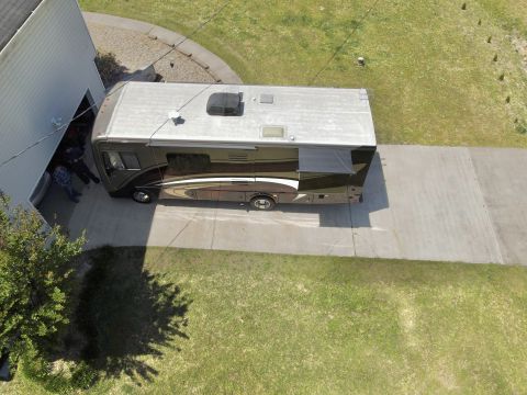 2015 Ford F-550 - An aerial view shows a large RV parked on a concrete driveway next to a white garage. The RV is dark brown with a lighter brown and white g…