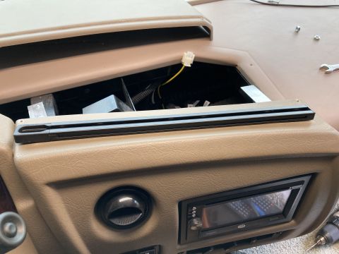 2015 Ford F-550 - A close-up view of a tan dashboard with a car stereo installed. A black trim piece is mounted above the stereo, and wiring is visible in an…