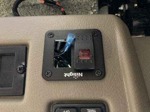 2015 Ford F-550 - A close-up view of a black Nilight brand rocker switch with a red illuminated button, installed in a tan dashboard. The switch has multiple…