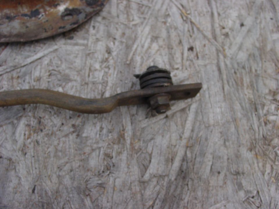 Rusty metal lever arm with spring and bolt assembly on a flat plate.